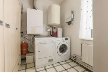 Funkcjonalne pomieszczenie gospodarcze z pralką, suszarką, bojlerem i szafą.