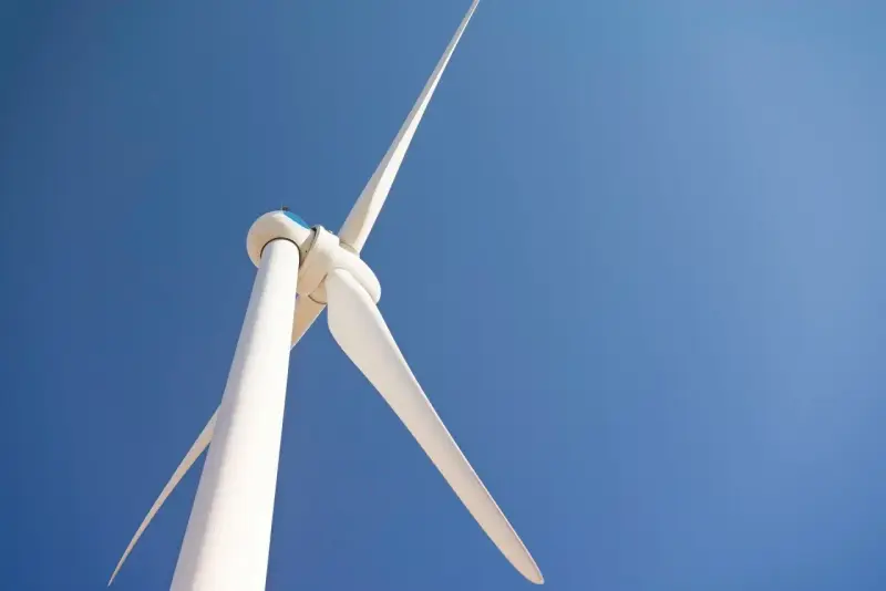 Białe turbiny wiatrowe obracają się na tle błękitnego nieba, czerpiąc energię z wiatru.