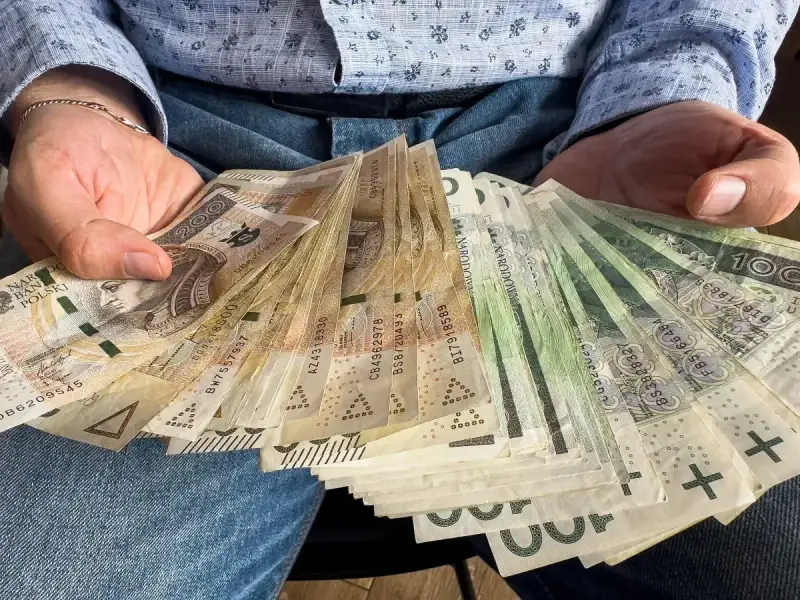 Ręce trzymające plik banknotów 100 zł i 200 zł. To może być darowizna 100 tysięcy od rodziców na nowy dom.