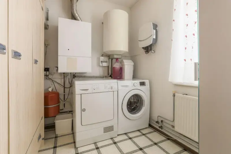 Funkcjonalne pomieszczenie gospodarcze z pralką, suszarką, bojlerem i szafą.