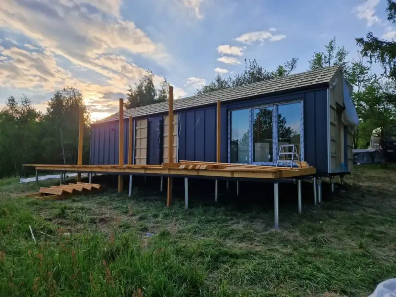 Nowy bungalow na palach, z drewnianym tarasem i dużymi oknami, w trakcie budowy.